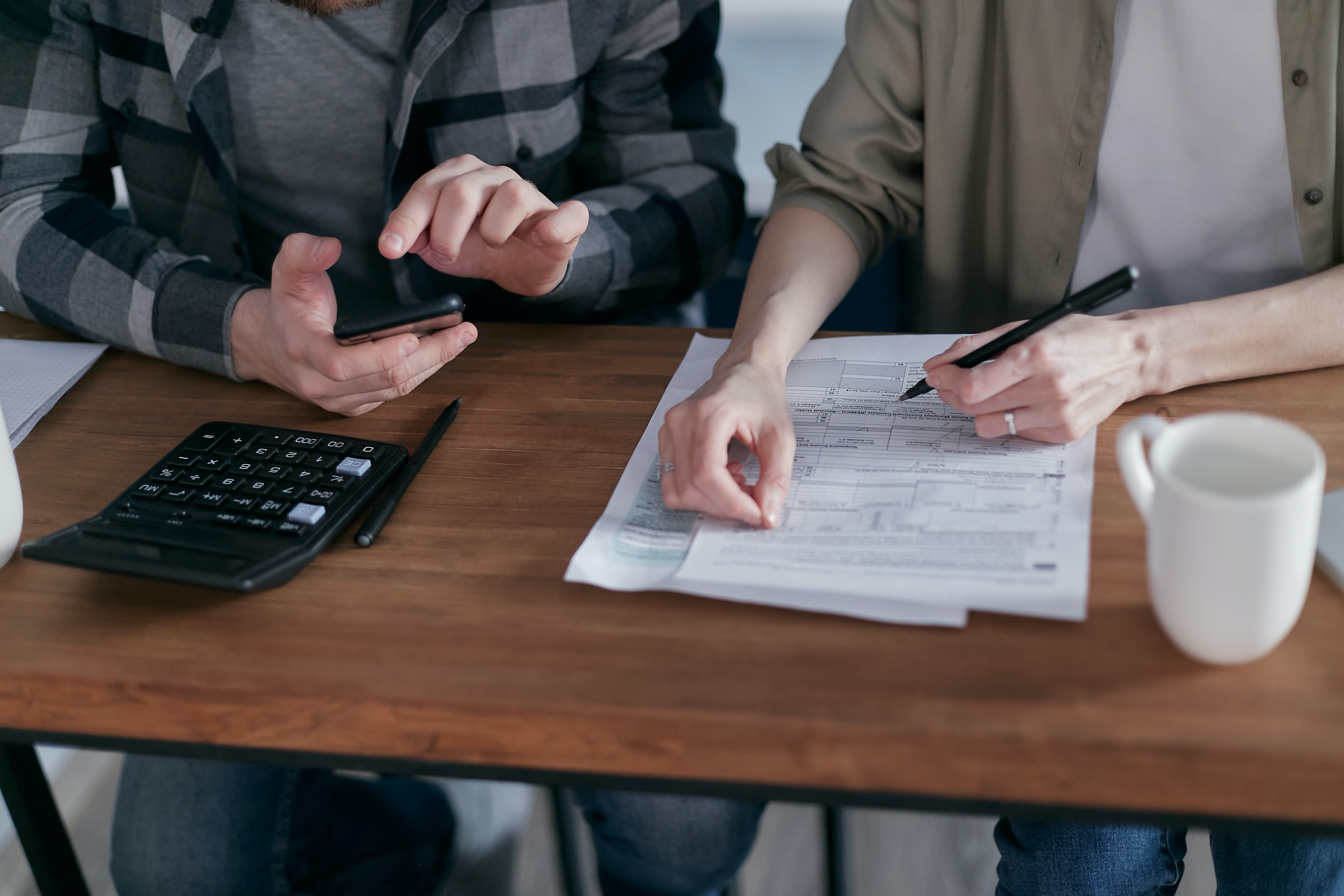 Two people sitting at a table with a calculator, filling out a form.