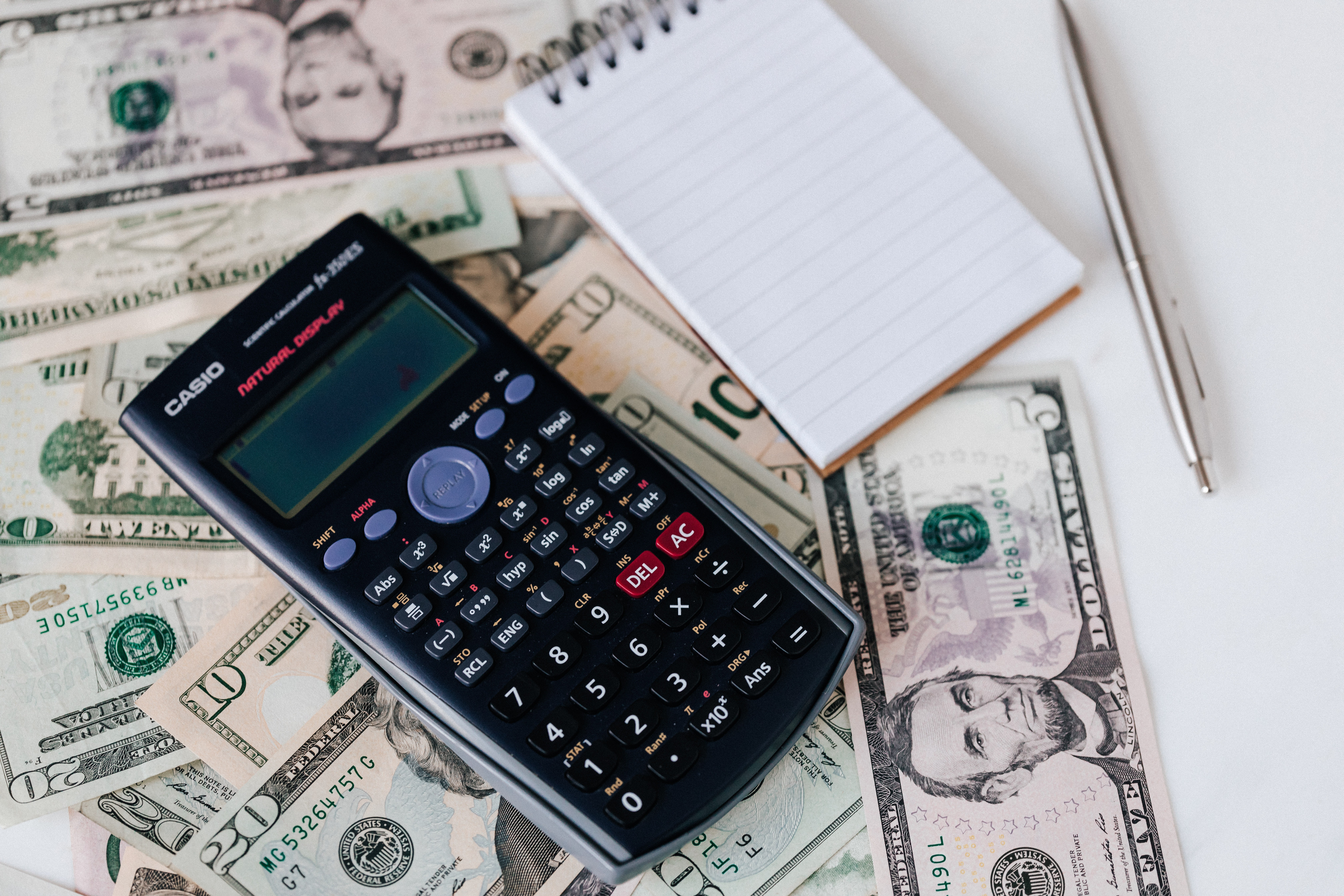 A calculator sitting on top of cash next to an empty notebook.