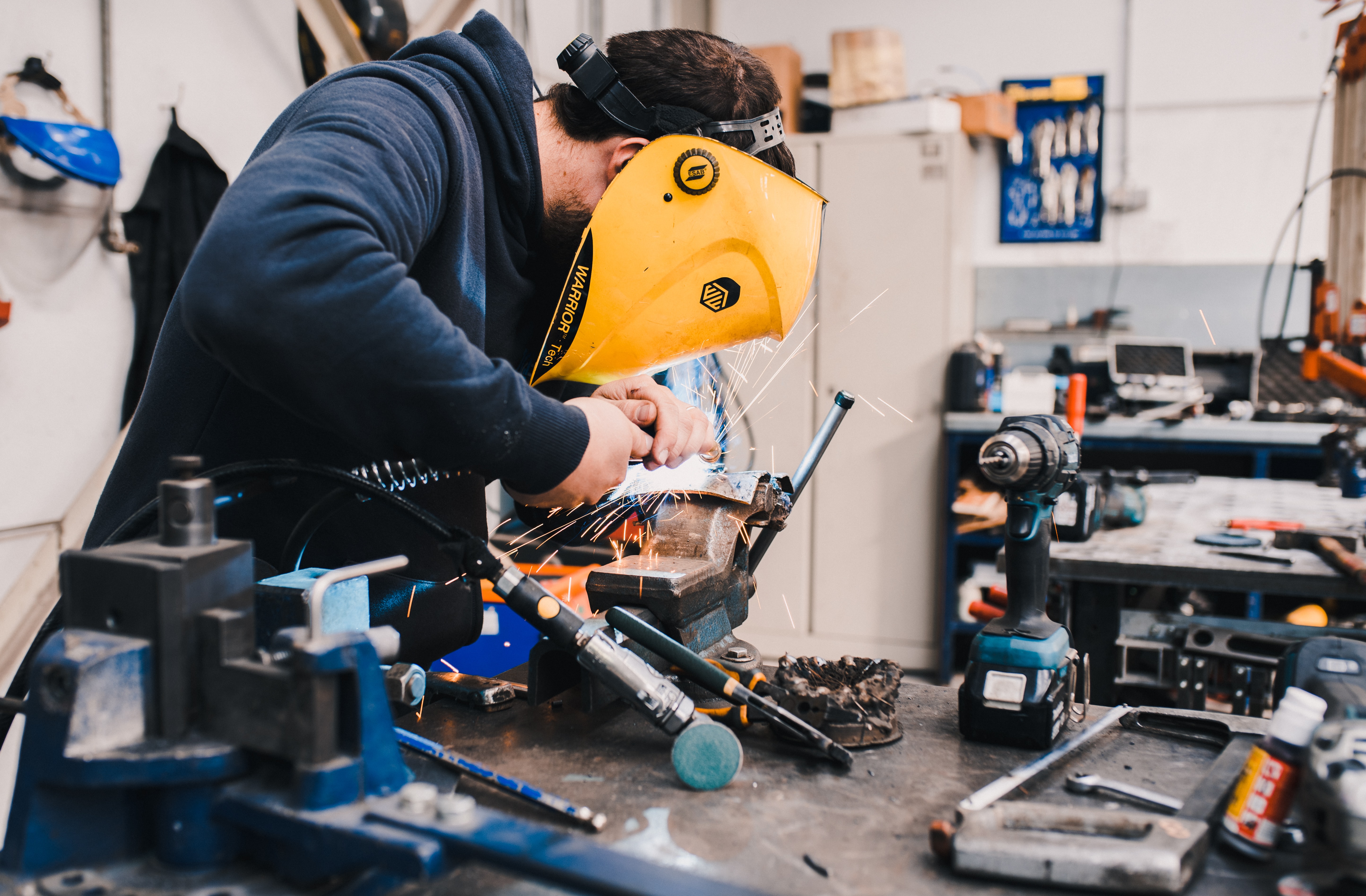 A medium closeup photo of a man welding or using a grinder on a workbench wearing a yellow welders facemask.