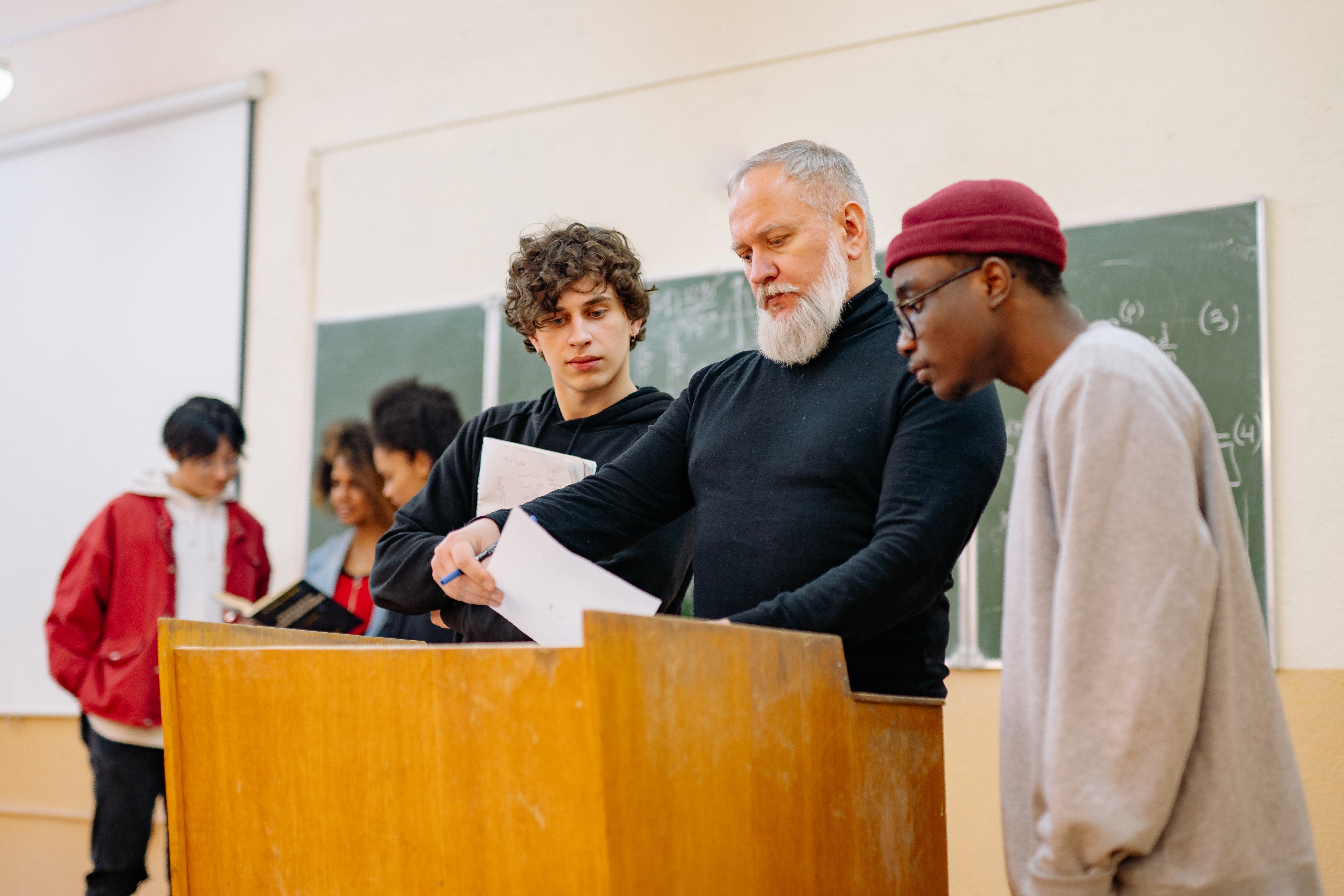 A professor showing two students a paper, standing at a podium.