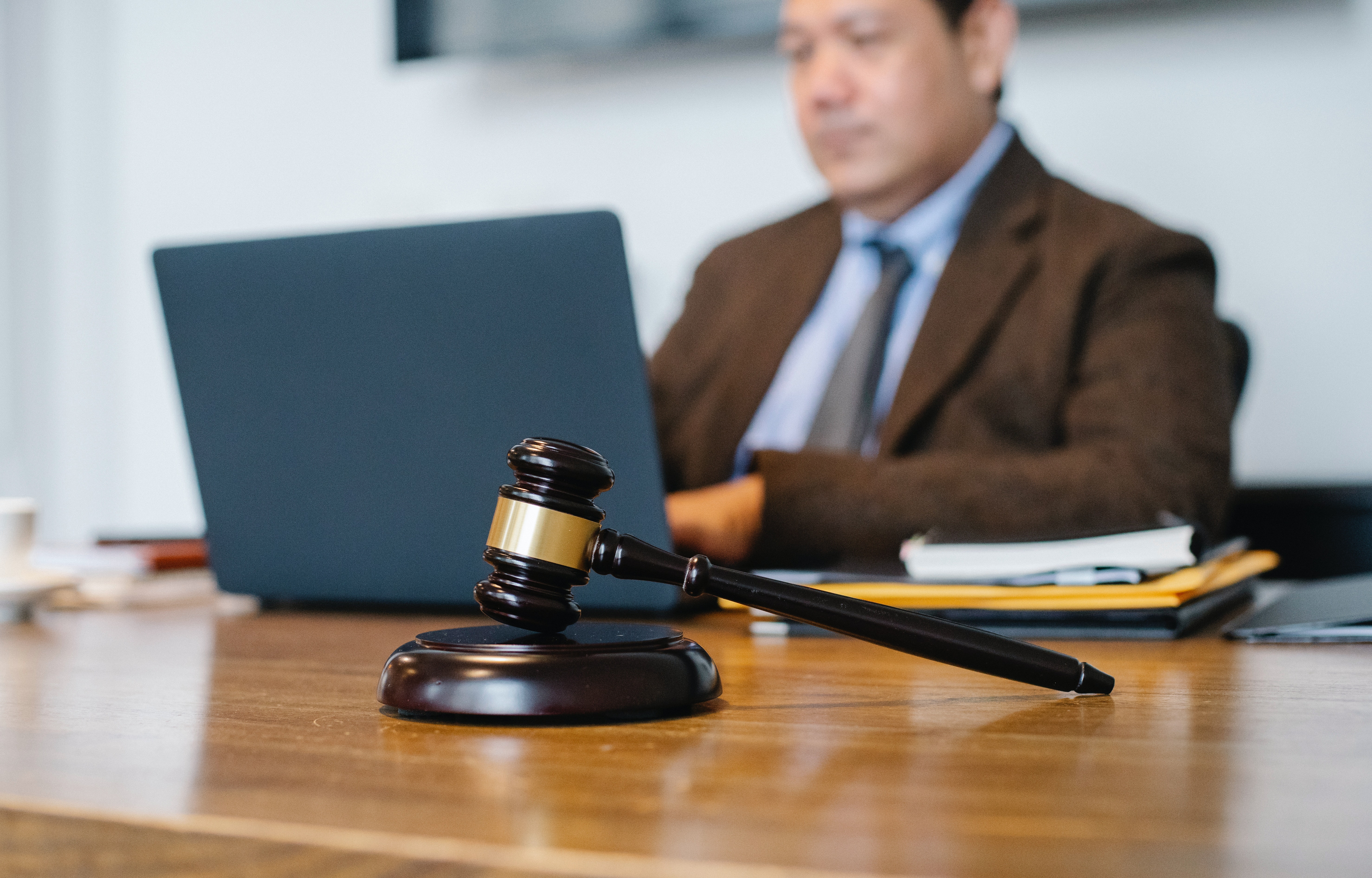 A close up photo of a man, in a busienss causal suit, sitting at his desk working at his laptop computer with a gavel in the foreground.