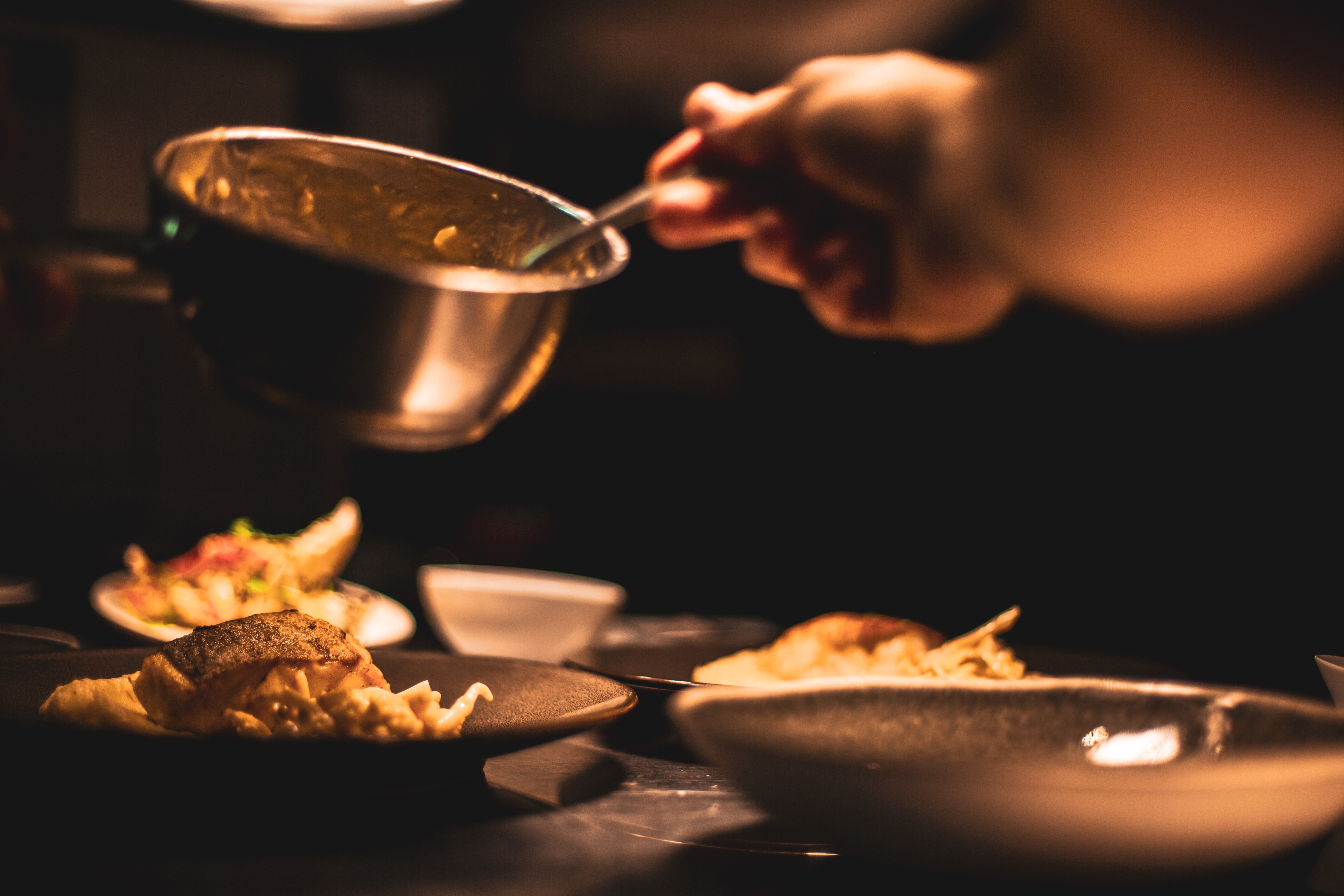 A person spooning something from a pot onto plates with various food items.