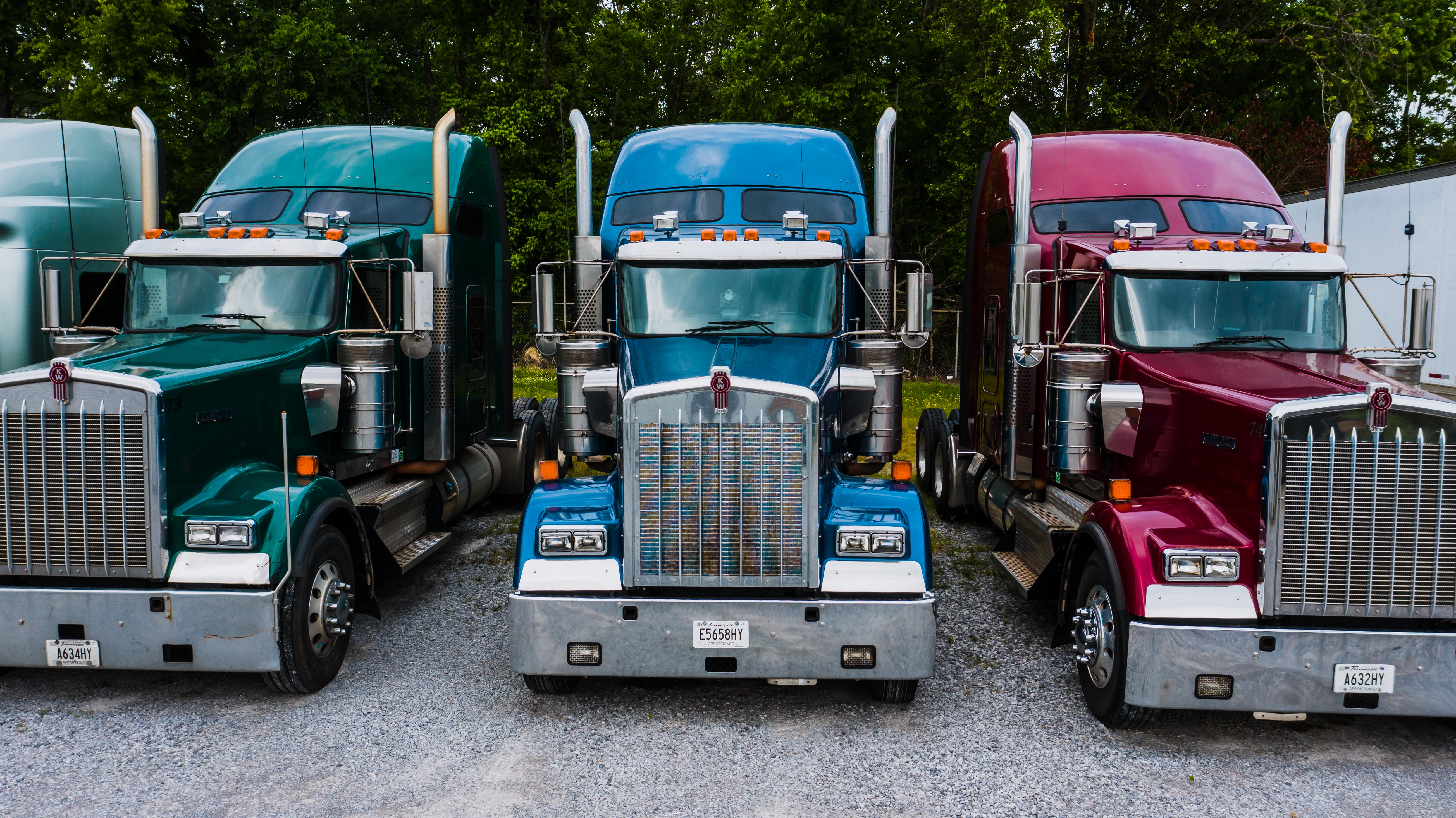 A close up photo of the fronts of a series of diesel trucks with each in a different color: green, red and blue.