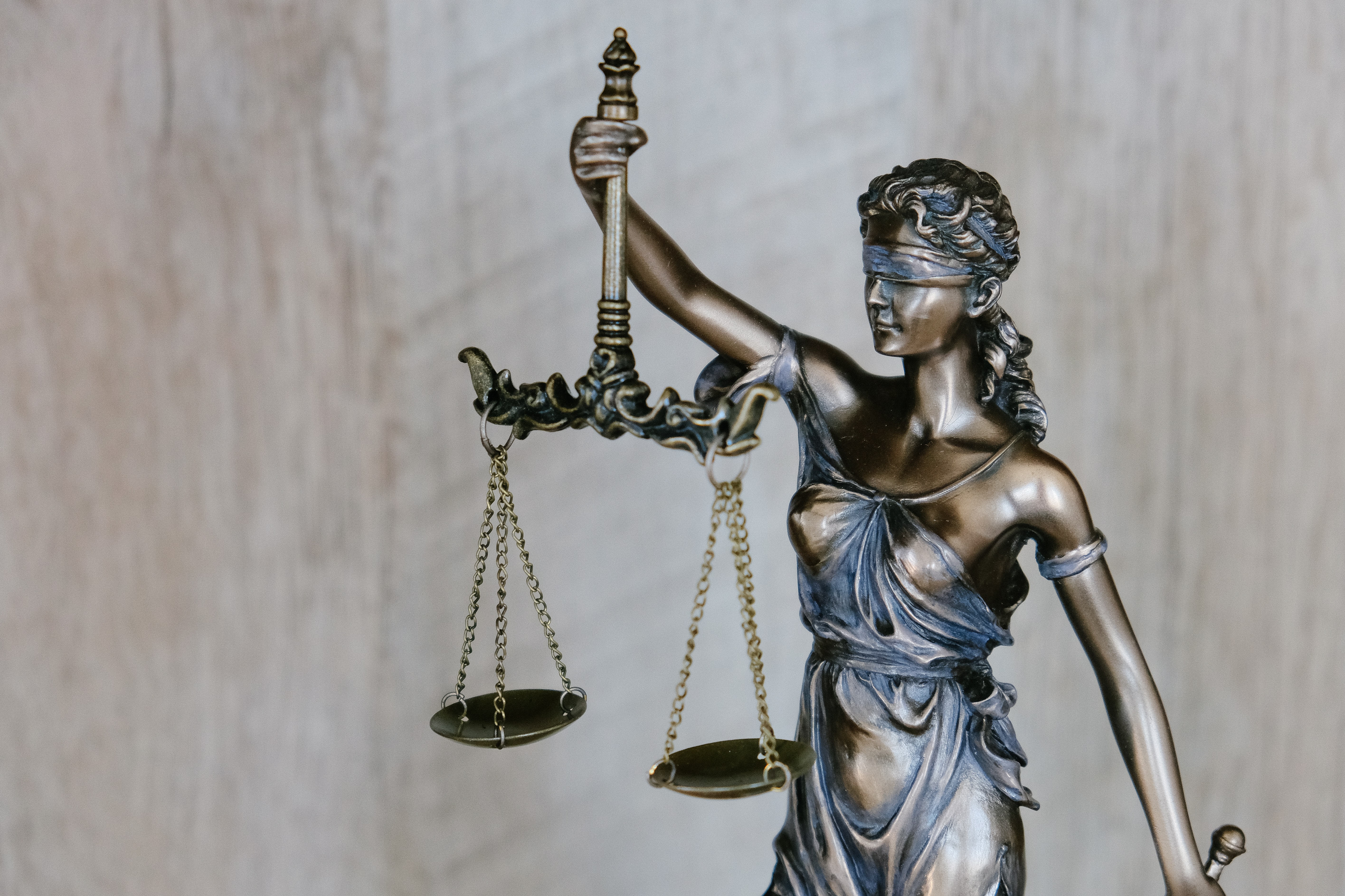 Photo of a silver statue of justice holding the scales of justice out with one hand