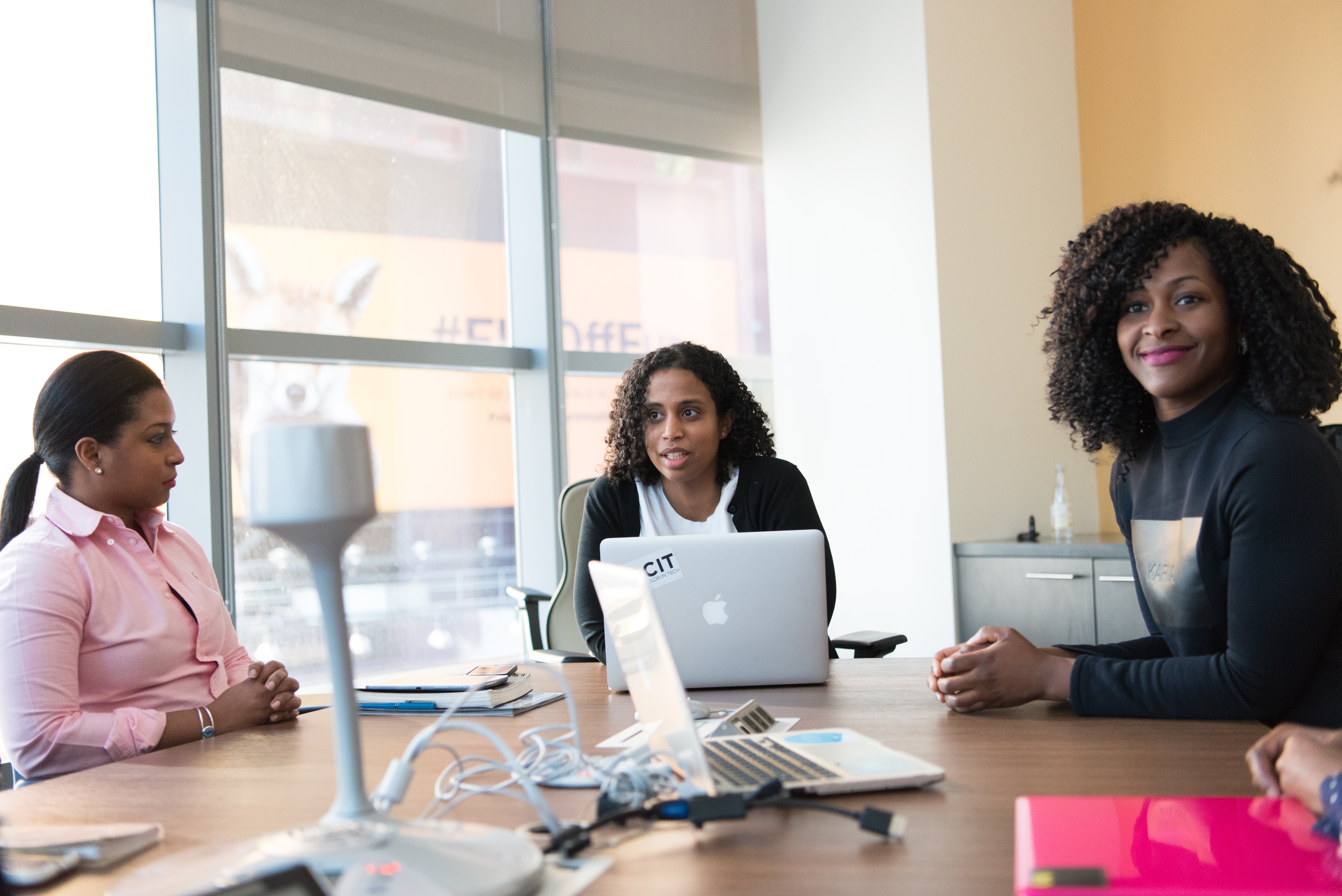 A photo of three ladies sitting at an office conference table with a couple of laptop computers who could be paralegals.