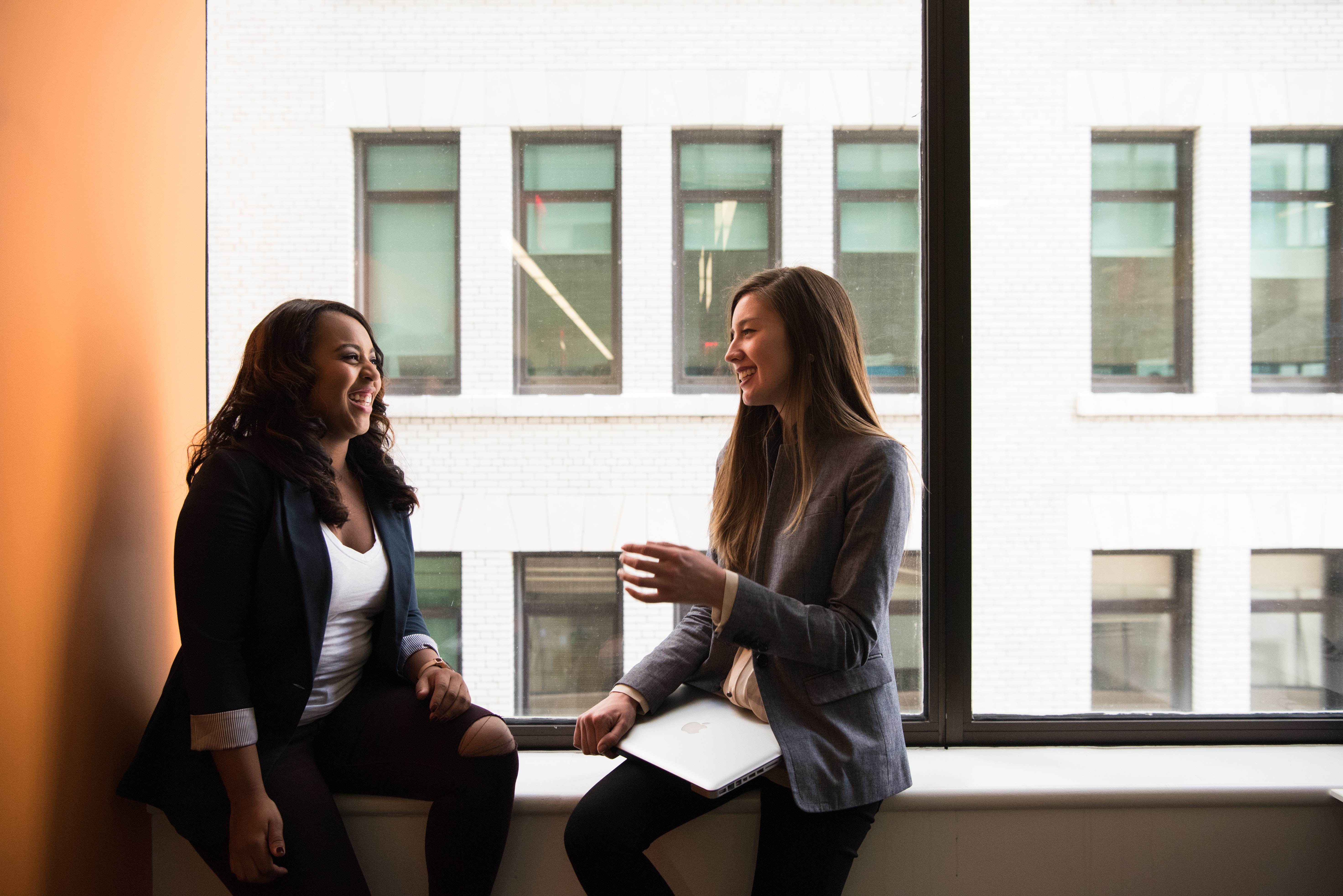 A photo of couple of ladies, who could be paralegals, sitting in an office window talking.