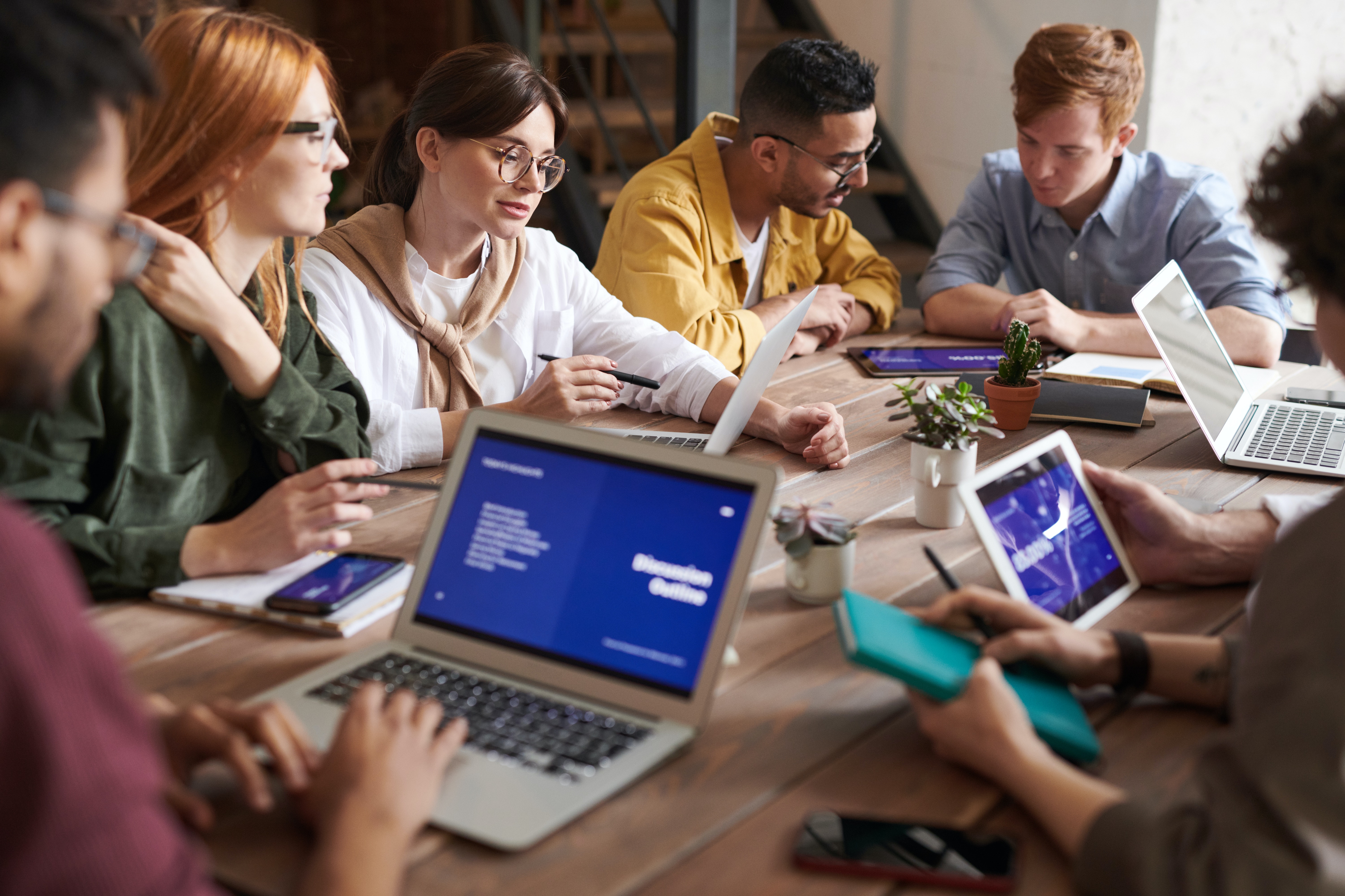 A photo of 4 young people, casually dressed, sitting at a table in an office meeting with notepads and a laptop computer.