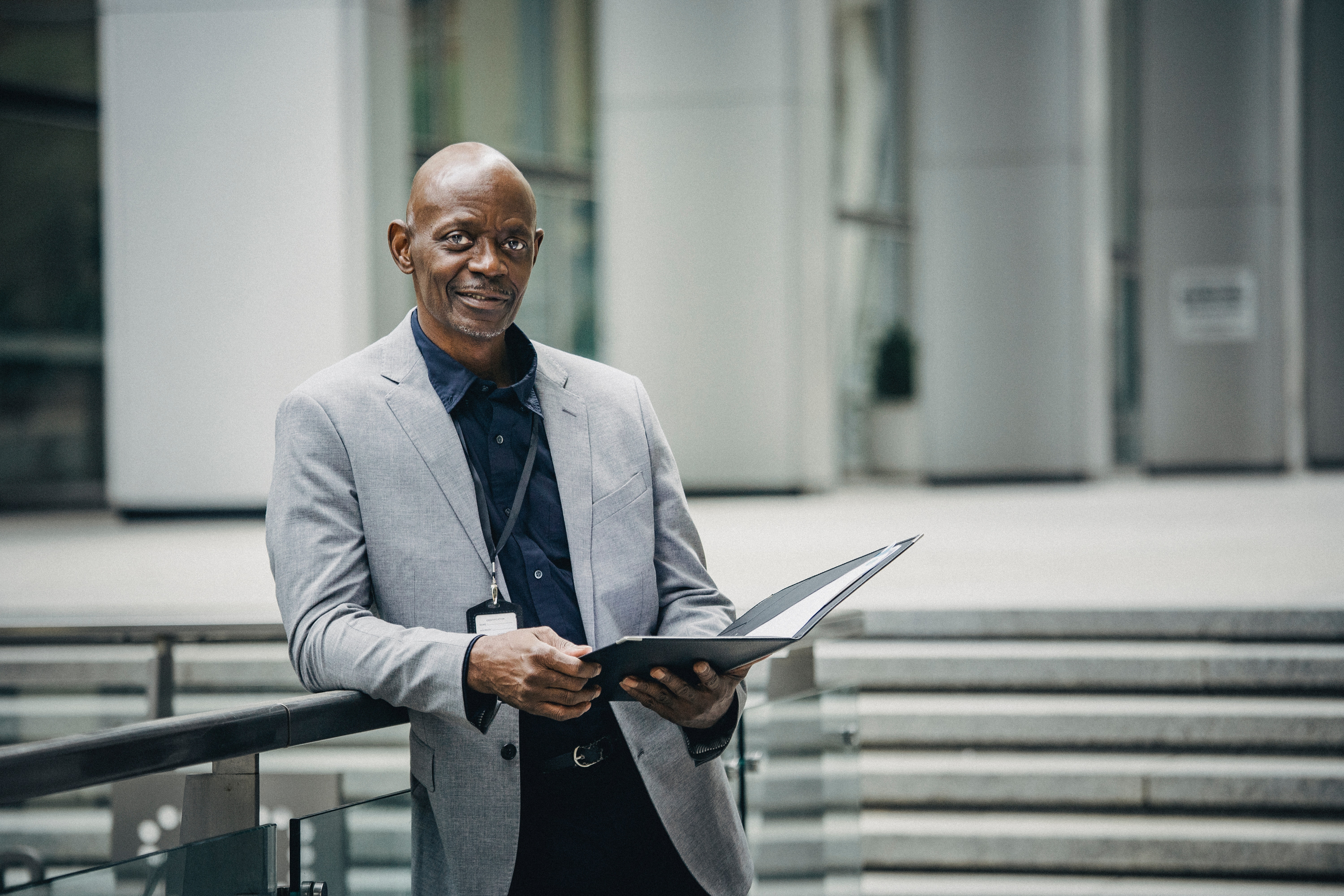 A long medium closeup photo of a man, who could be a manager, leaning against a railing with an open black folder.