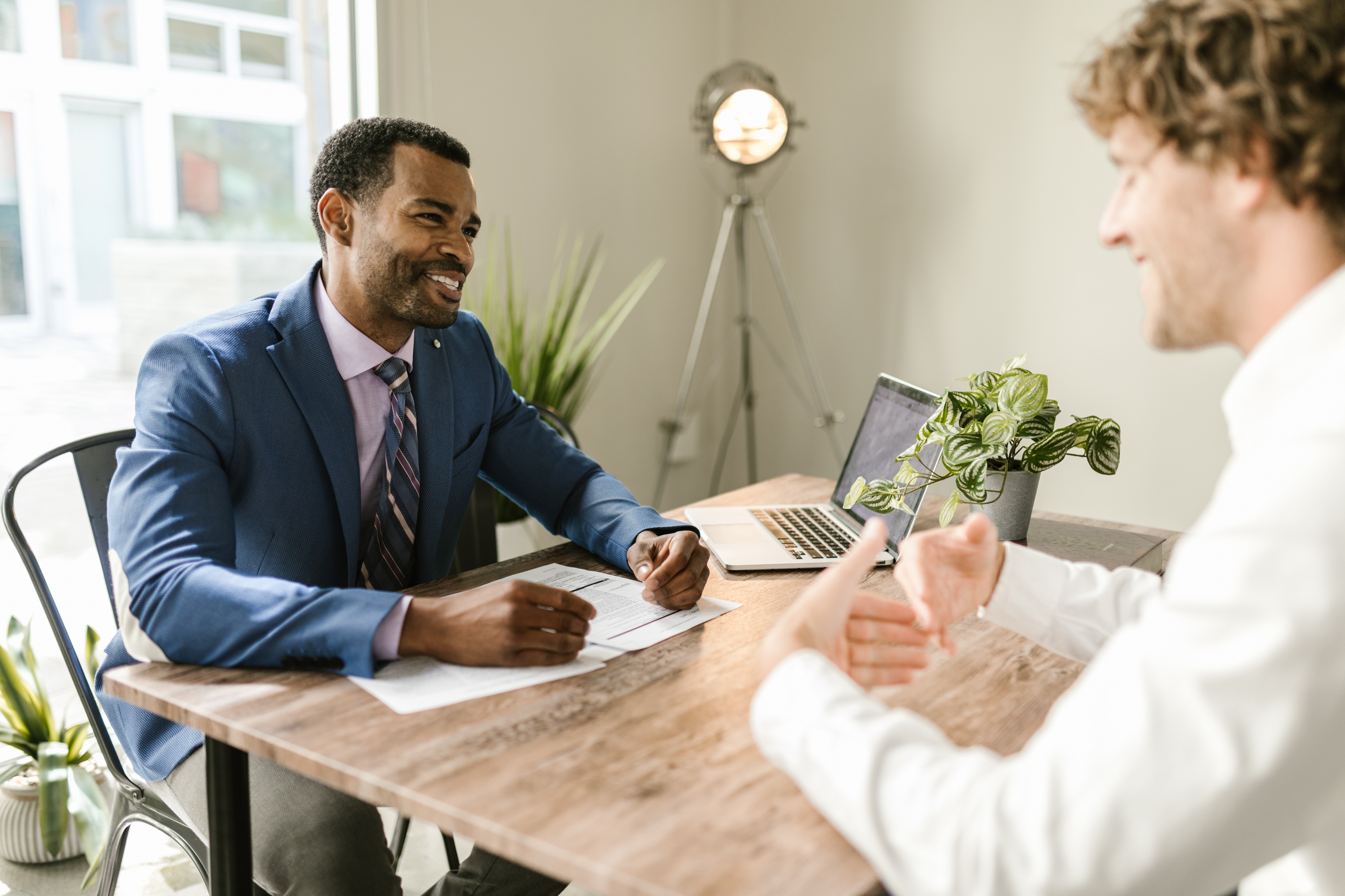 A photo of an accountant and one of his clients sitting at a table meeting. Both men are smiling and it appears this meeting is takiing place at the client's residence.