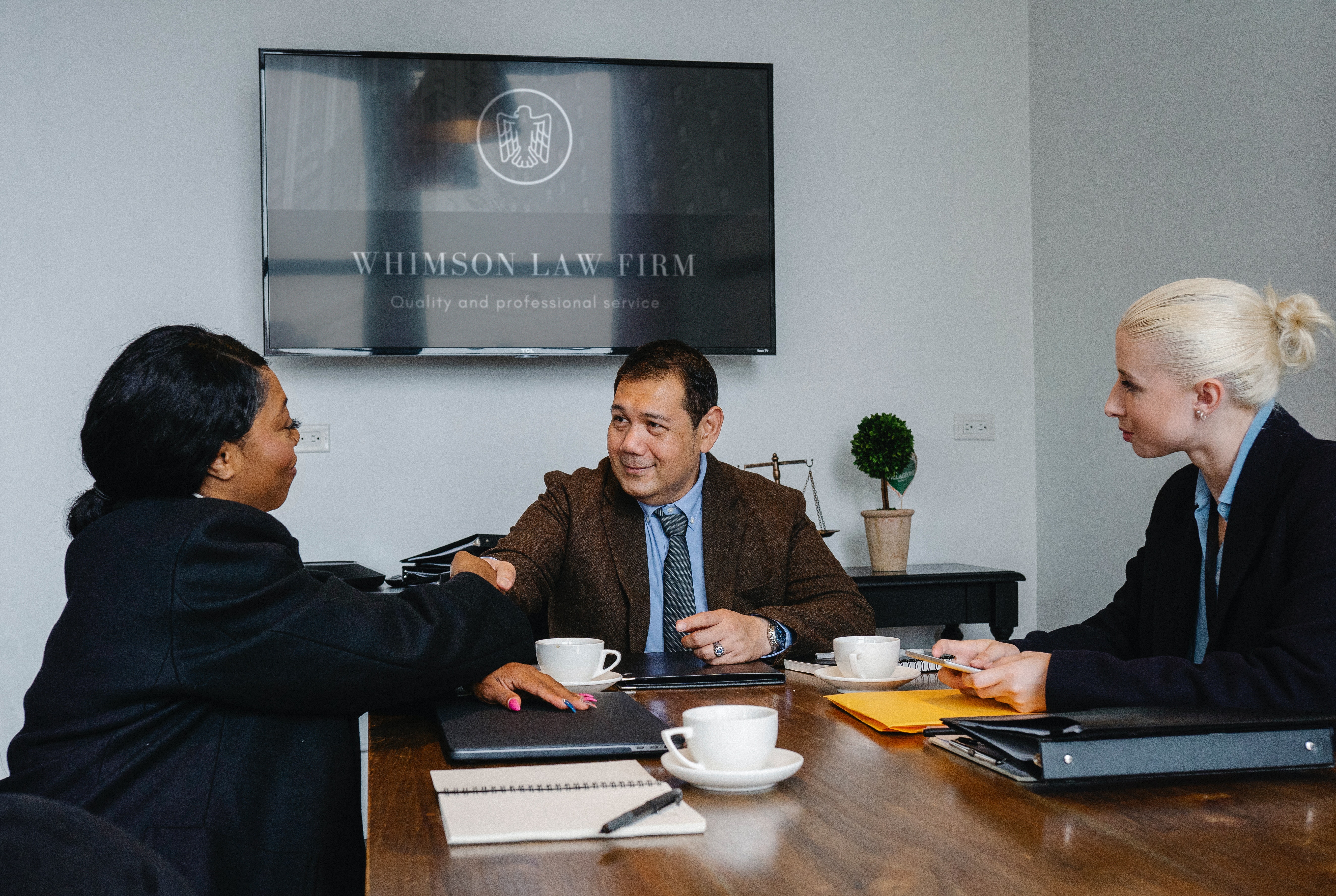 A photo of a meeting with an attorney and his paralegal, who is a lady, shaking hands with one of his clients, who is a lady, too.