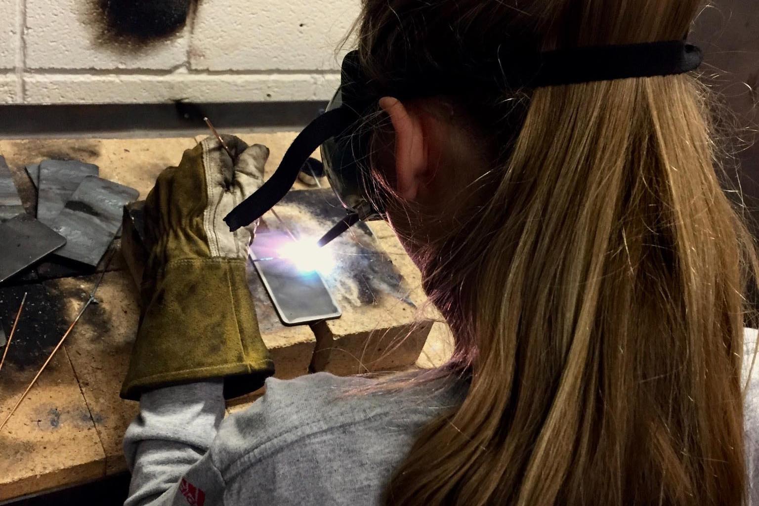 A picture of a woman welding at a workbench.